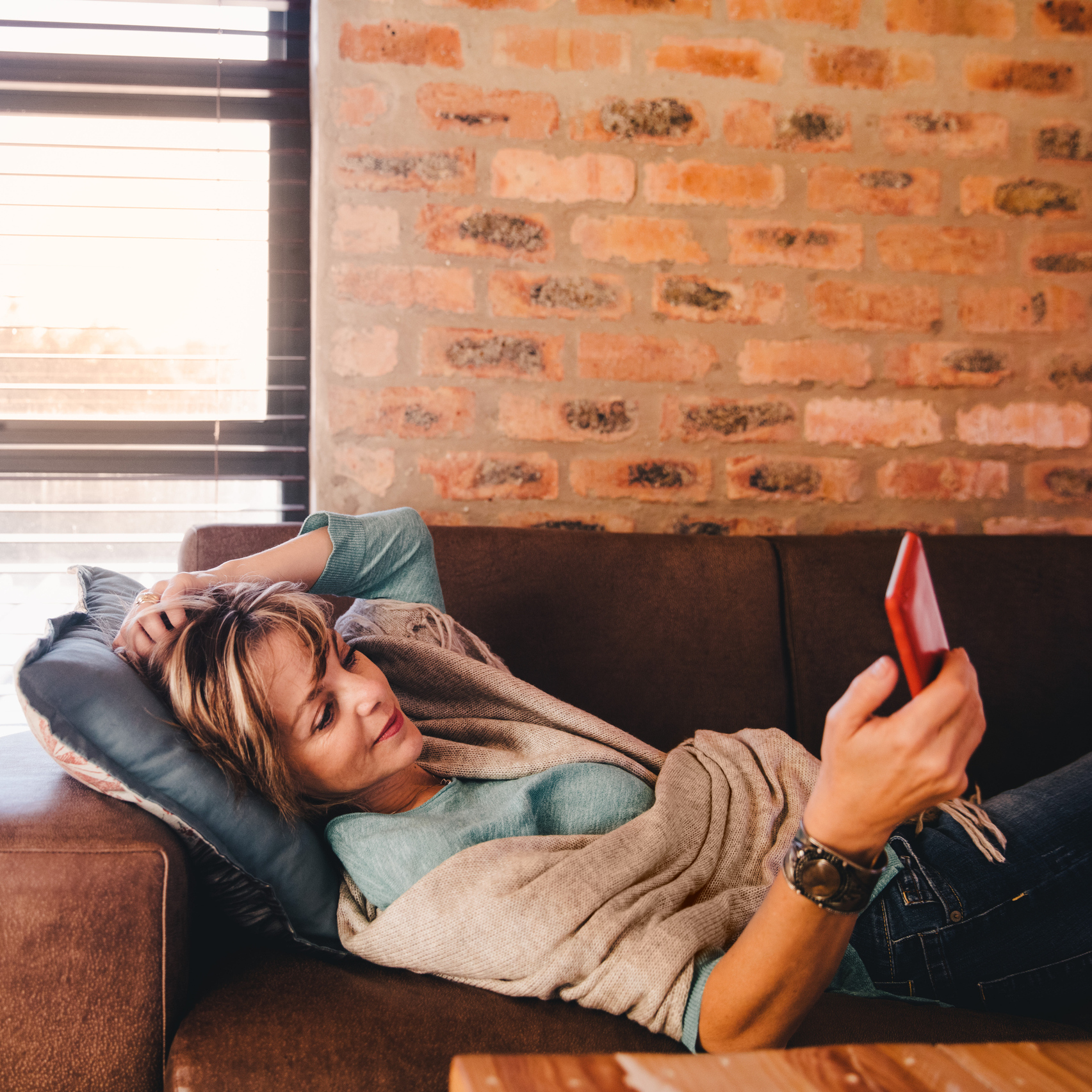 woman lying on her couch looking at her phone