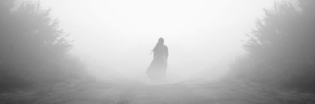woman walking down a foggy road in the forest