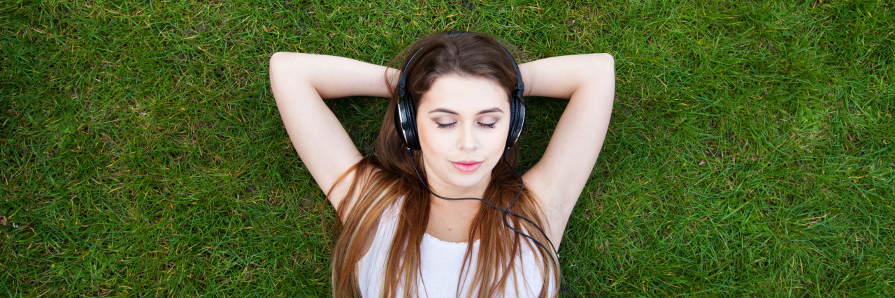 Woman in the grass wearing headphones.