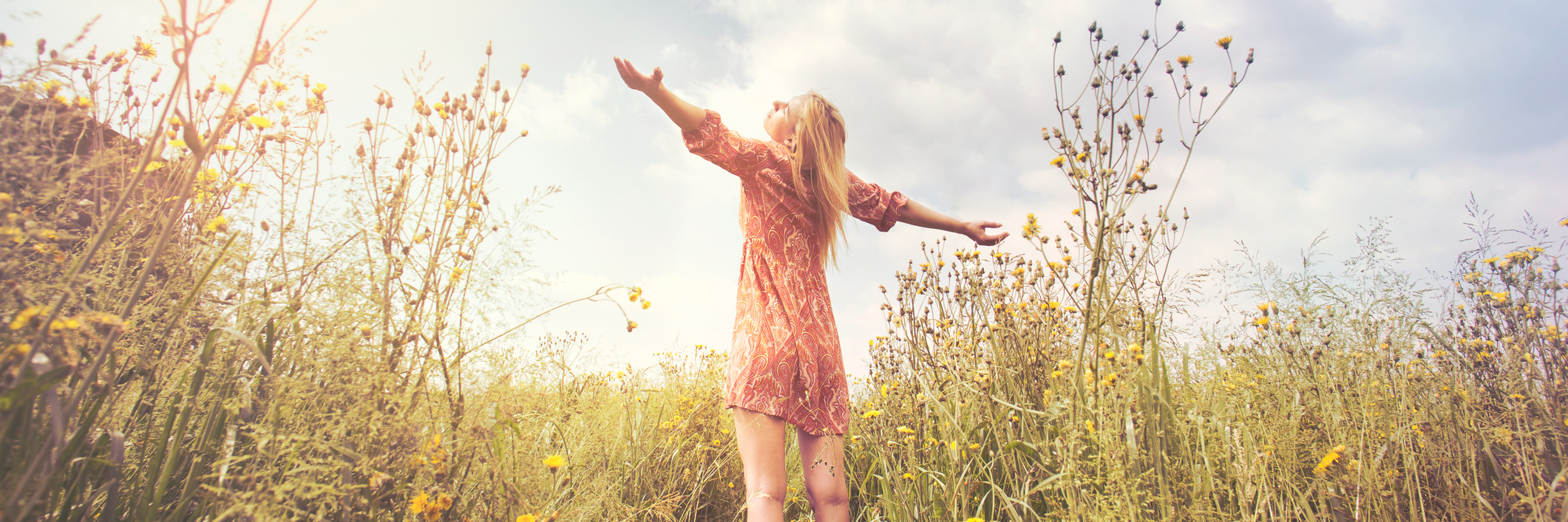 Woman standing in field with outstretched arms, blue sky above her