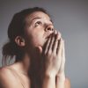 upset woman with tears in eyes and praying against gray background