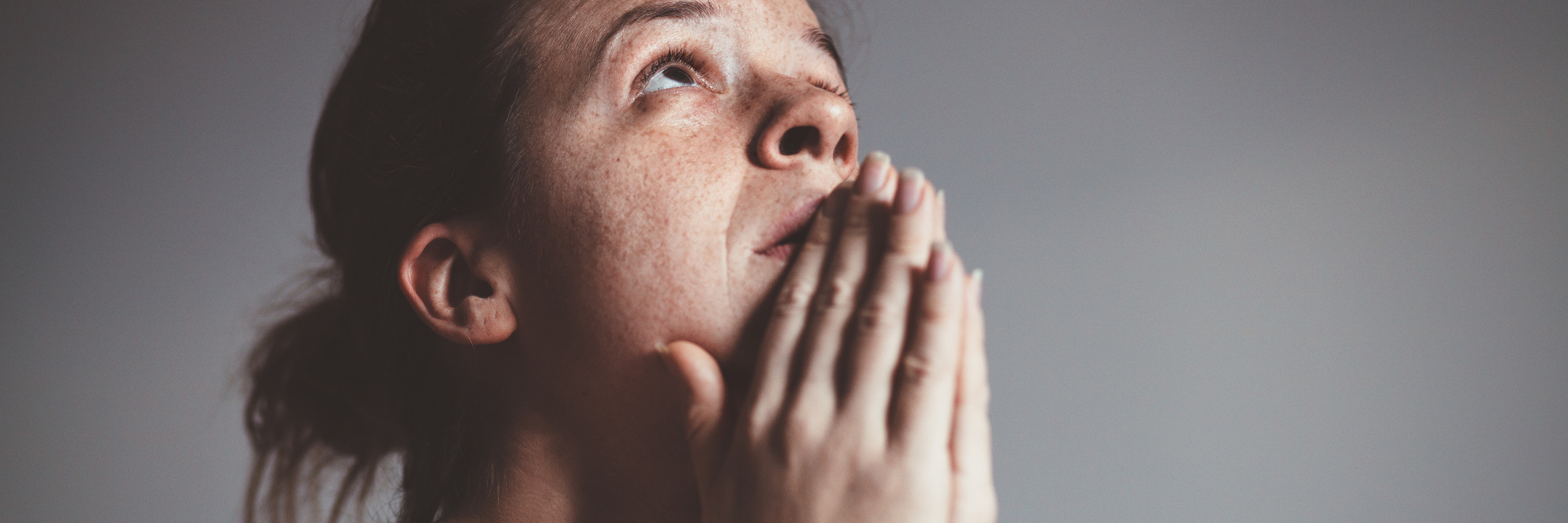 upset woman with tears in eyes and praying against gray background