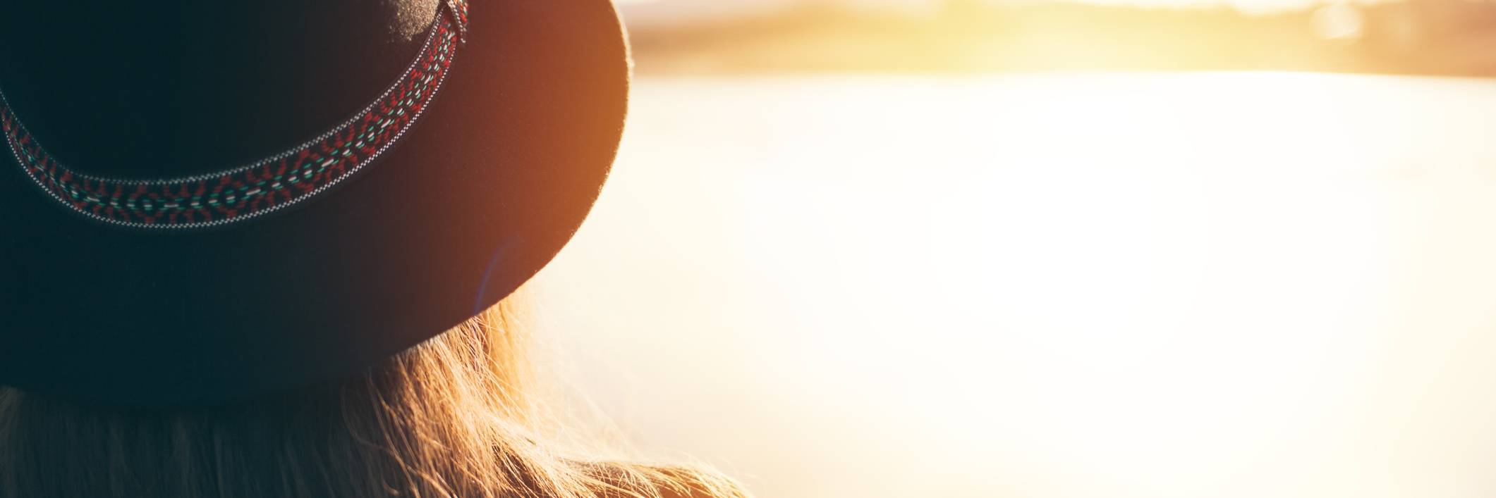 Constantly Being Reminded of Your Chronic Illness woman wearing a hat and looking at the sunset over a lake