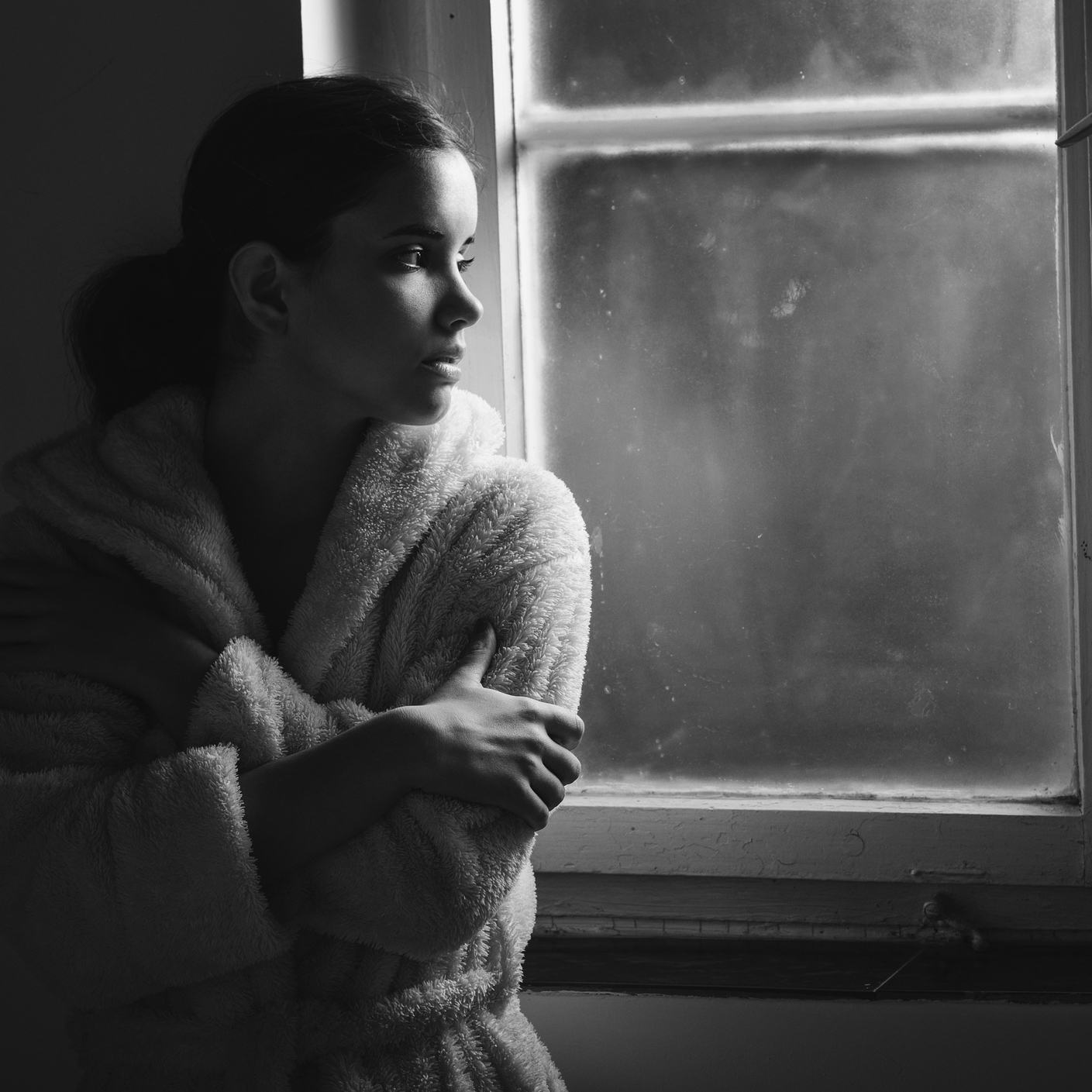 black and white photo of a woman standing next to a window