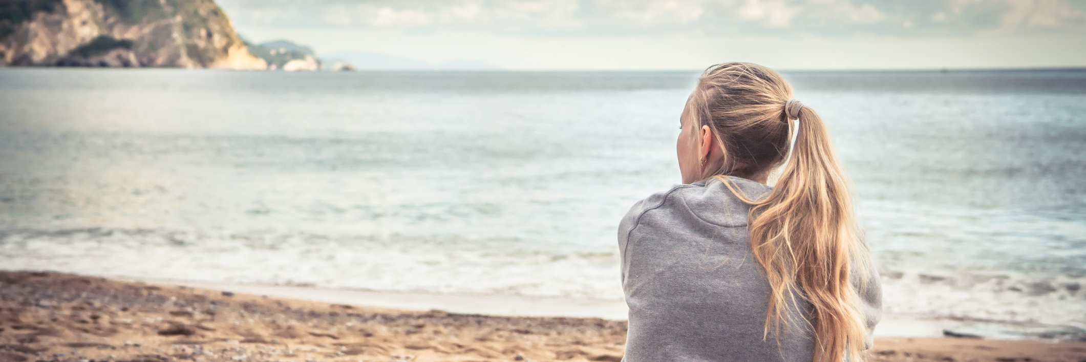 Pensive woman sitting on beach hugging her knees and looking into the distance with hope.