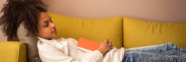 An young woman falling asleep on the couch with a book in hand.