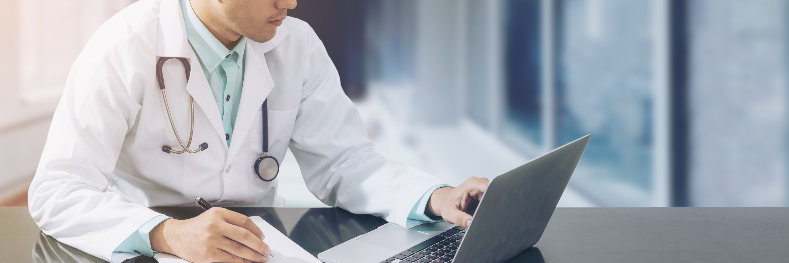 doctor looking at laptop and writing on a notepad