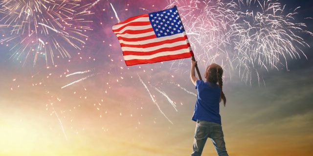 young girl waving an american flag in the sky with fireworks