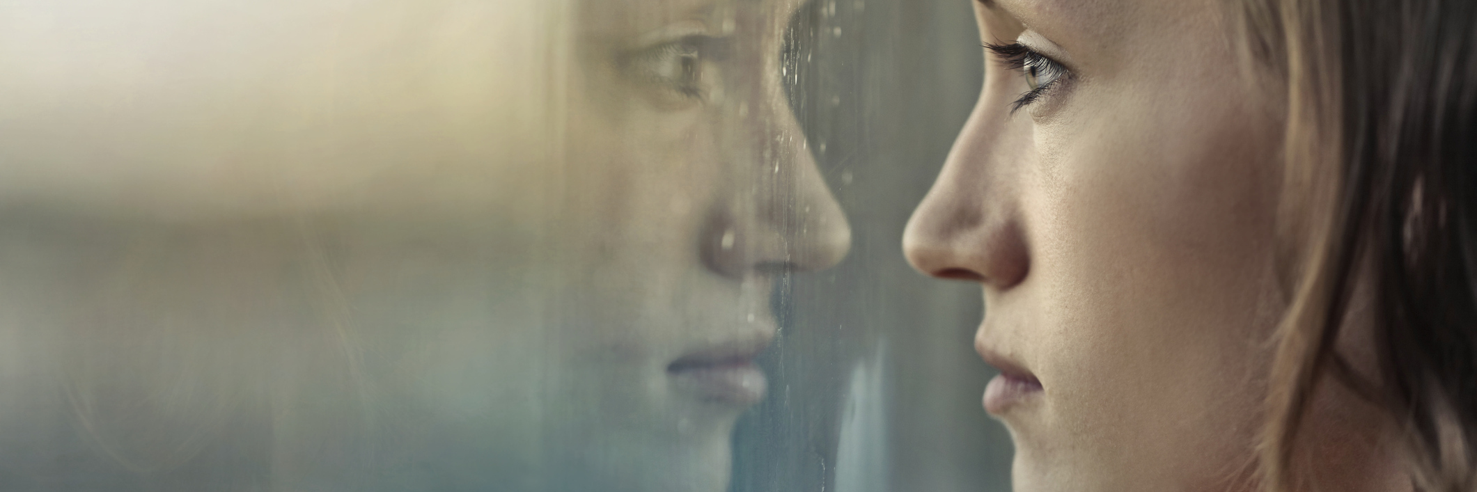 young woman looking through window with rain