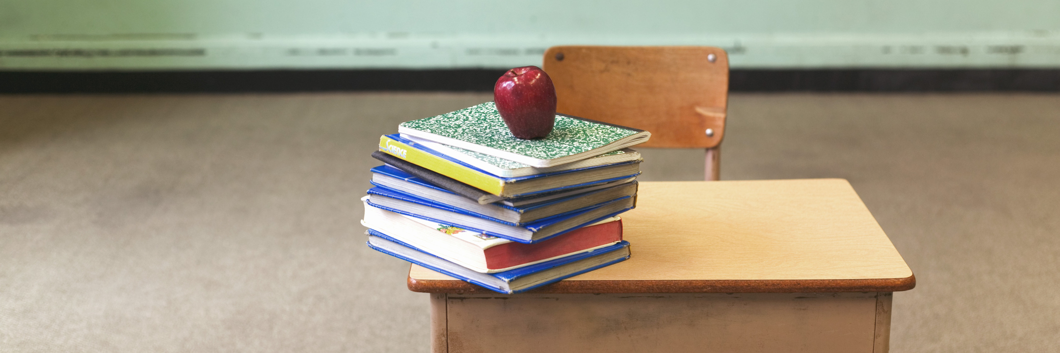Stack of school books and apple on desk in empty classroom