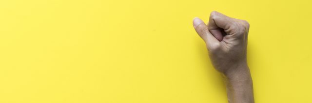 A females fist clinched on a yellow background.