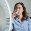 woman drinking water and sitting in front of a fan