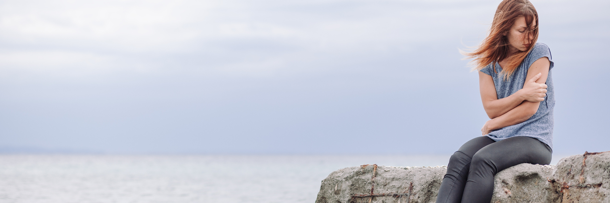 Things for Friends to Know About Borderline Personality Disorder woman alone at seaside sitting on rocks looking depressed arms folded