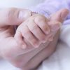 woman's hand holding baby's hand on sheets