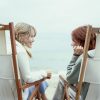 two women sitting in chairs on the beach and talking