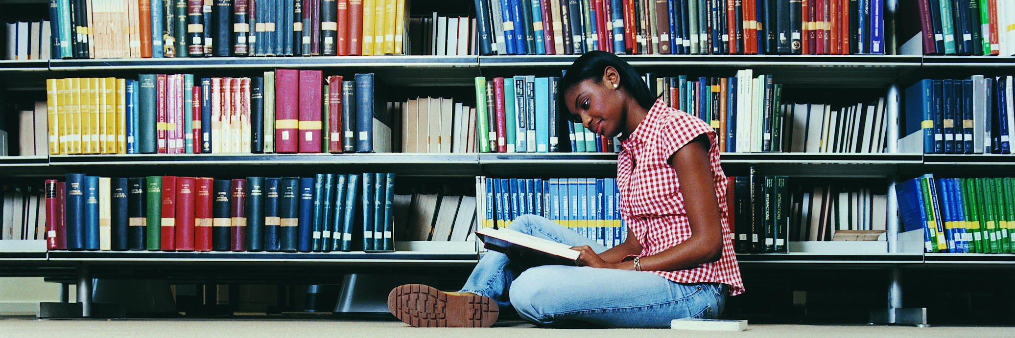 Female University student sitting in library reading a book.
