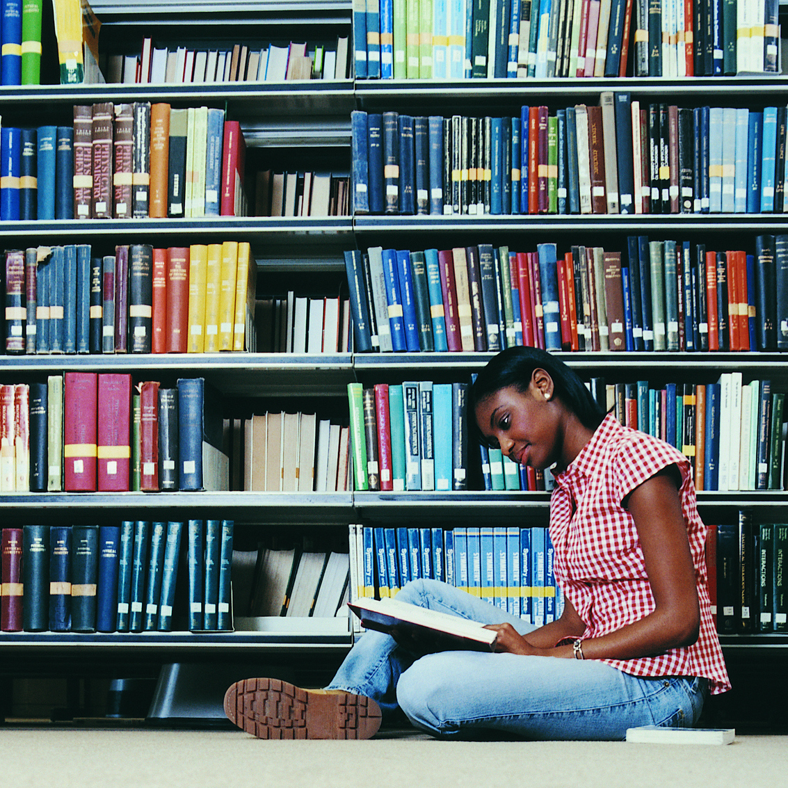 Female University student sitting in library reading a book.