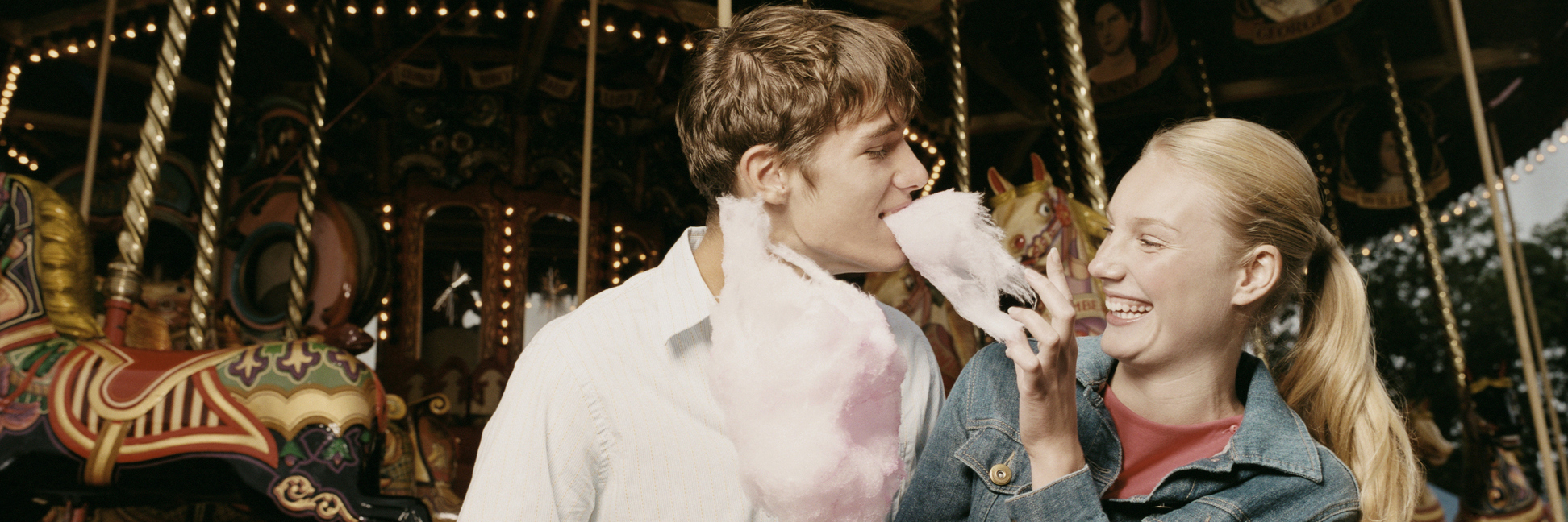 A young couple on a date, eating popcorn and standing in front of a ride.