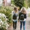 two girls wearing backpacks walking down the street together