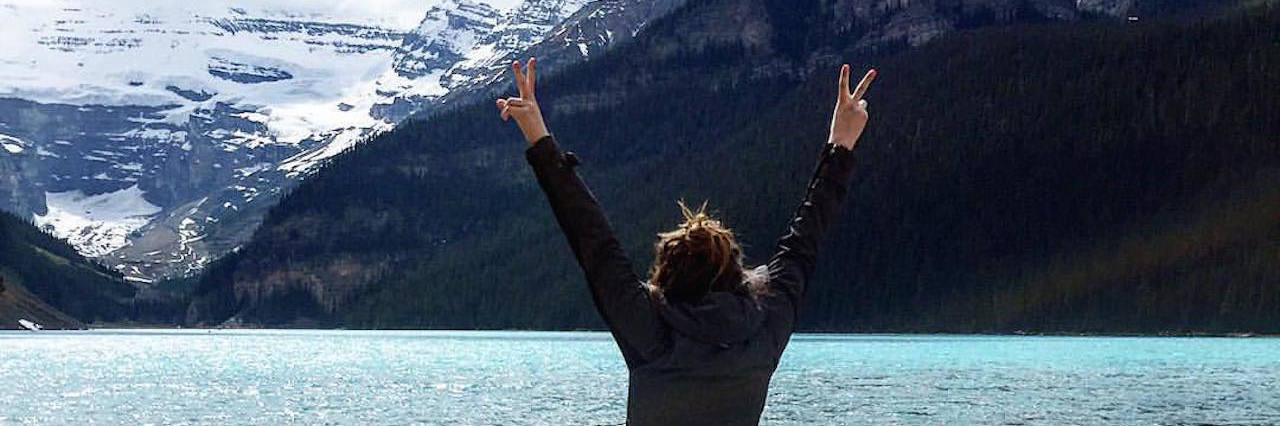 A woman with her hands up standing in front of a lake