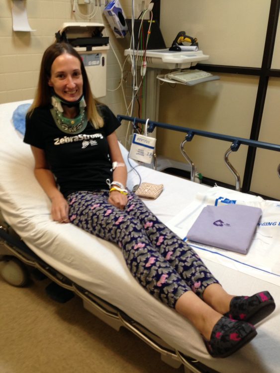 The writer sitting on a hospital bed while wearing a neck brace.