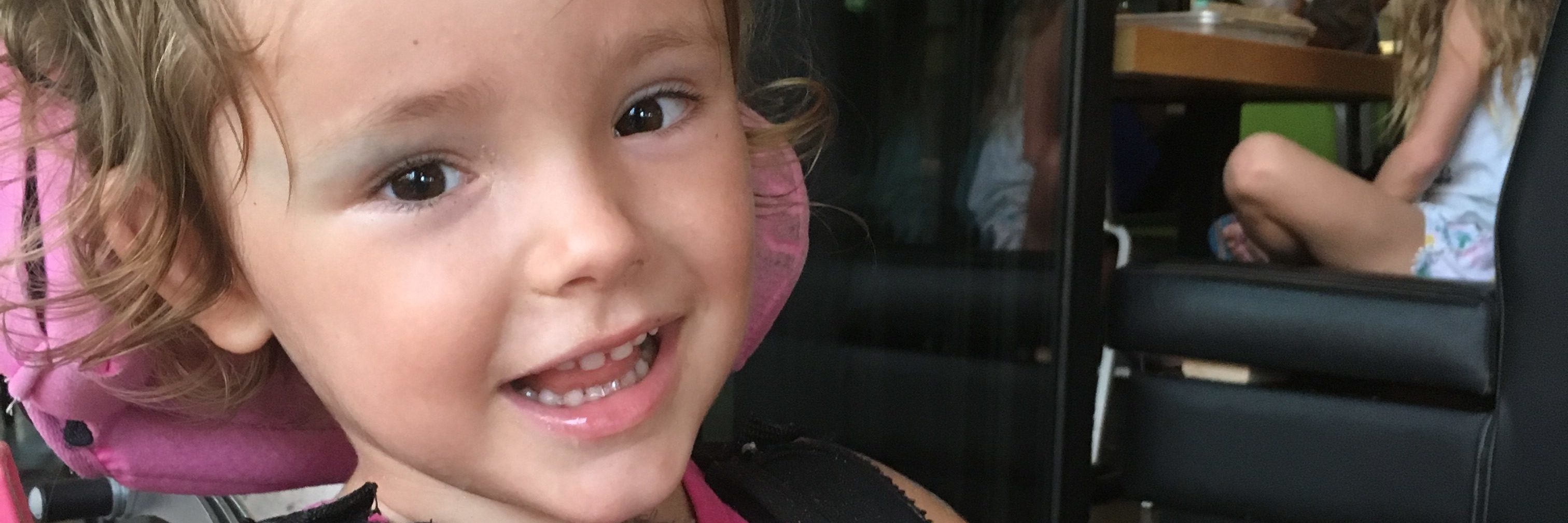 Why There Are Children Alone in Their Hospital Rooms Little girl wearing a harness, sitting on adaptive chair smiling at the camera