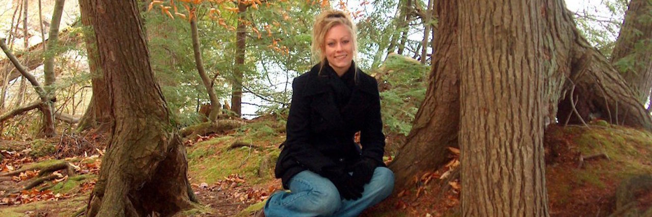 woman sitting in the forest next to a tree