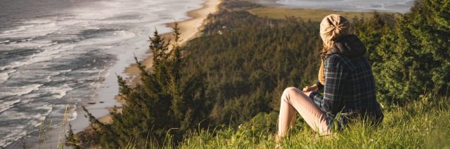 woman sitting outdoors in nature overlooking coastline and forest