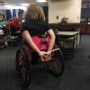 Disability rights activist Stephanie Woodward sits in her pink manual wheelchair with her hands cuffed behind her back.