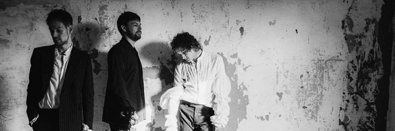 How The 1975's Music Help Me Cope With Anxiety three men from the band The 1975 in black and white stand looking down