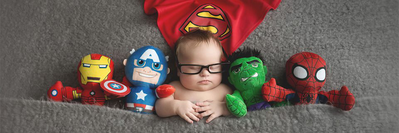 My Son With Down Syndrome Is 'The Rule Breaker' Bbay boy with Down syndrome wearing glasses, sleeping, superman cape above him while i the middle of stuffed superheroes
