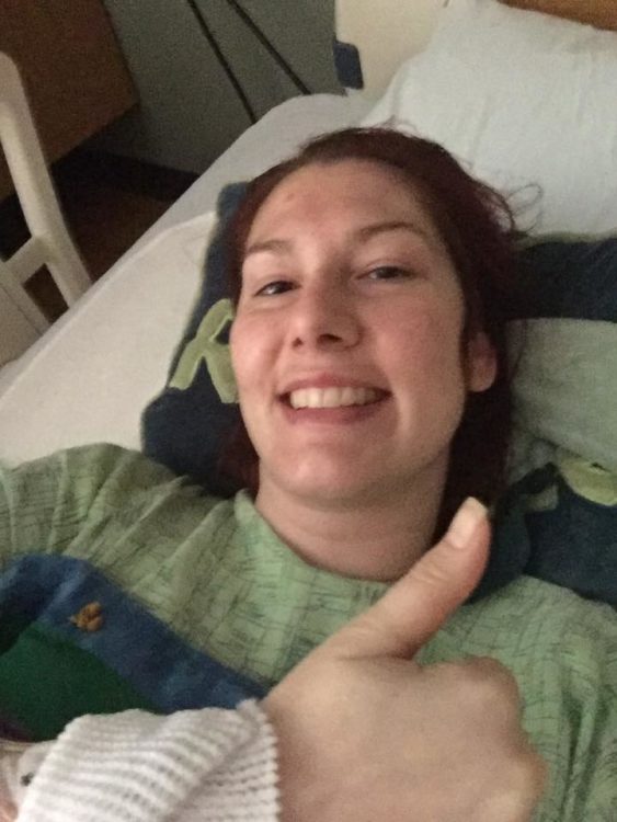 woman smiling and giving a thumbs up in a hospital bed