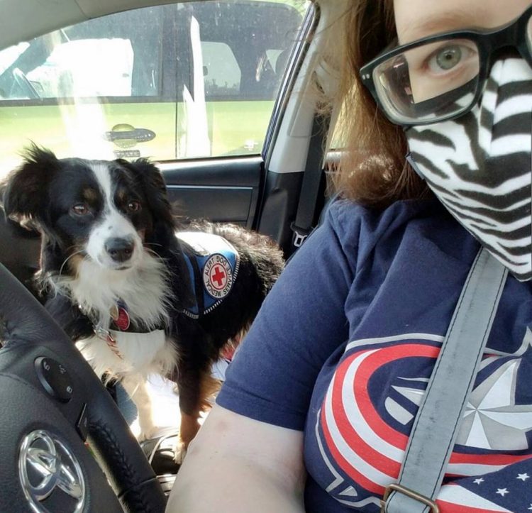 woman sitting in the car with her service dog and wearing a face mask