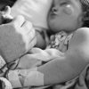 Black and white photo of little girl in hospital bed holding on to parent's hand while she sleeps