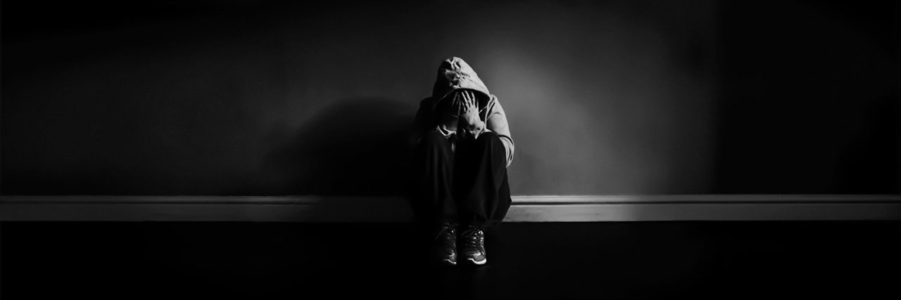How the Stigma Around Functional Neurological Disorder Affects Me black and white photo of person in darkness looking depressed against wall Michelle Tuttle - MCT Photography