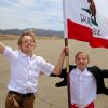 Two kids wearing white shirts and waving a flag.