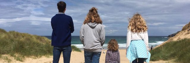 four kids standing on beach looking at ocean