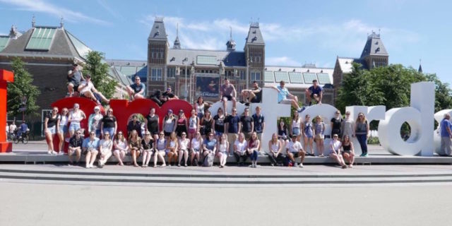 The Issues With Traveling Abroad When You Have an Autoimmune Disease group sitting in front of the 'I amsterdam" sign