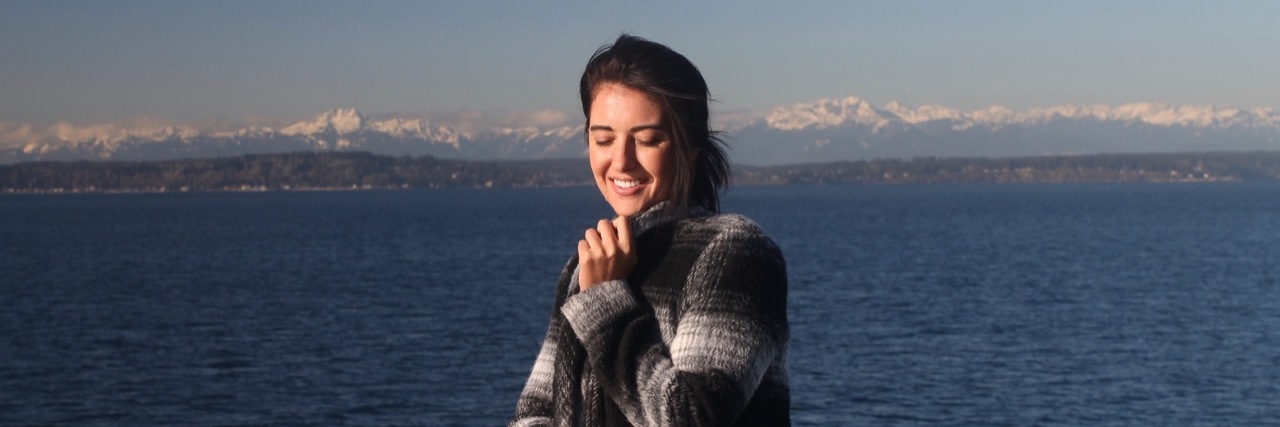 8 Tips for Getting Through College With Chronic Pain The writer standing in front of a body of water, smiling.