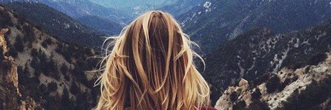 back of woman's head looking out over mountains and valleys