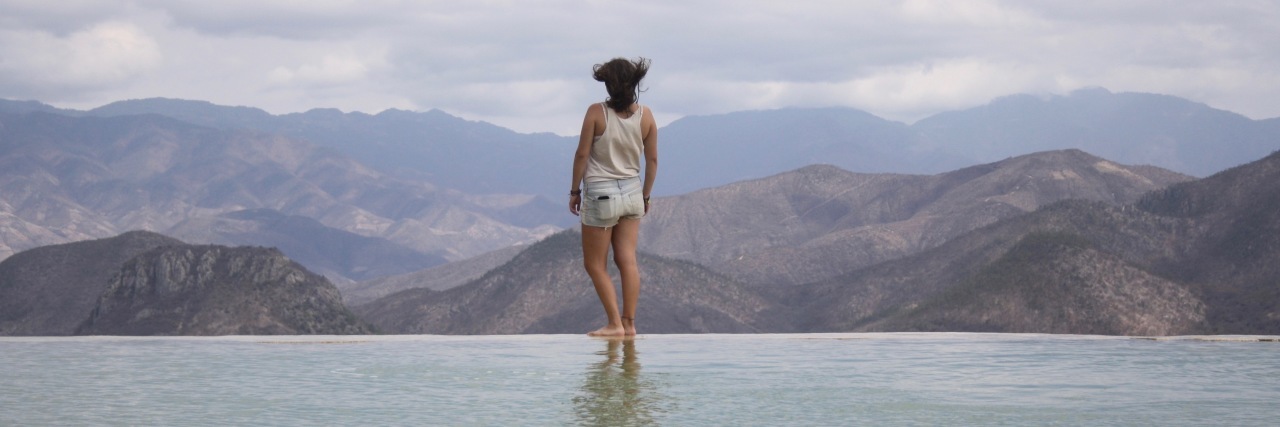 young woman standing on edge of water with mountains in background