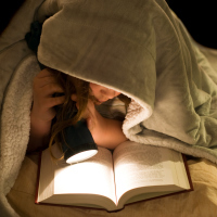 A young girl reading a book under the covers with a flashlight