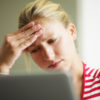 blonde woman with hand on forehead in front of computer looking upset or worried