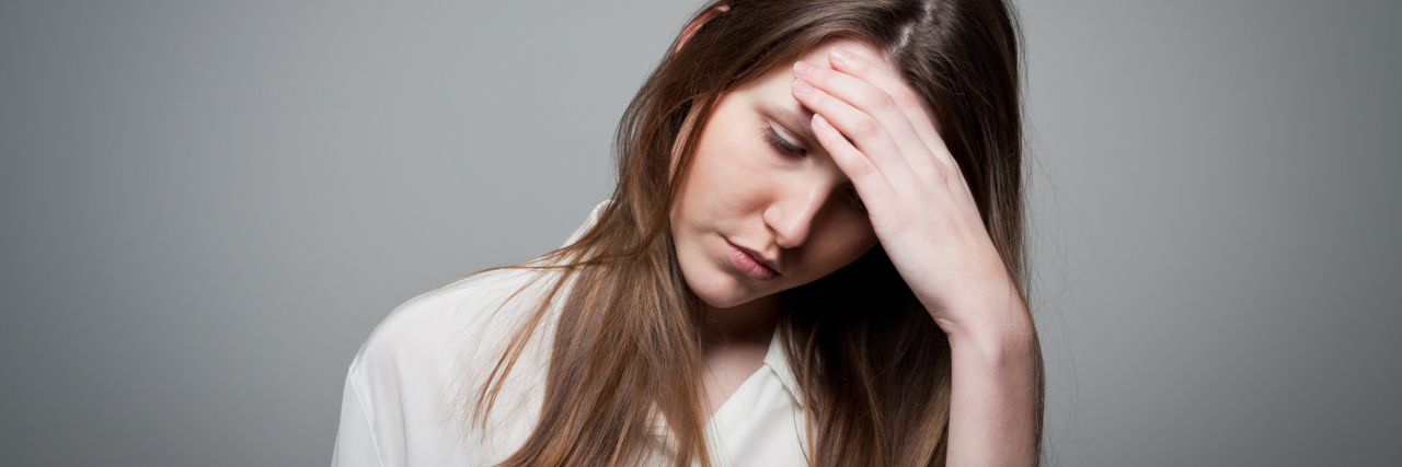 young woman against gray background with hand to head looking stressed and anxious