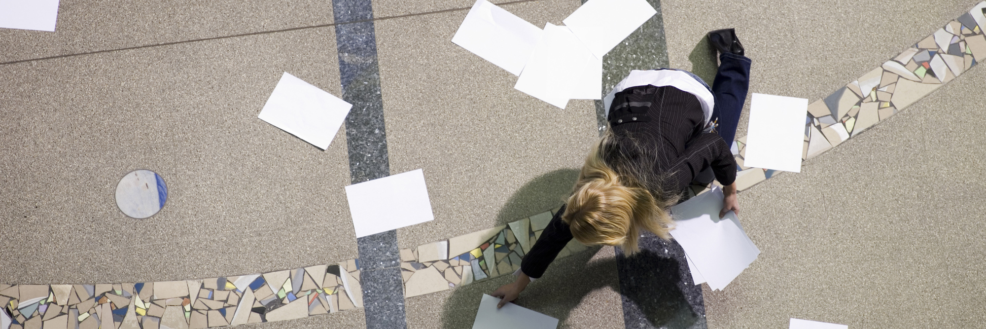 overhead view of blonde business woman in hall picking up scattered papers