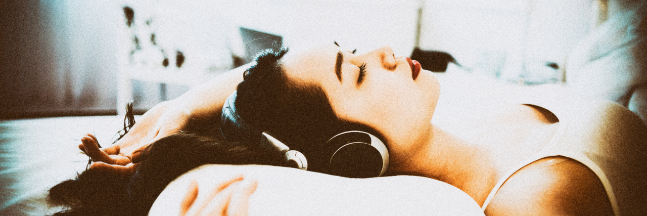 Asian woman lying in bed wearing headphones.