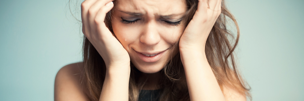 What I Need From You When I Have a Migraine A woman holding her head in pain, due to a migraine.