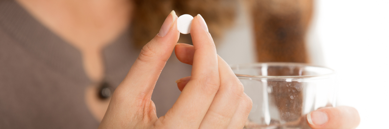 woman holding pill and a glass of water