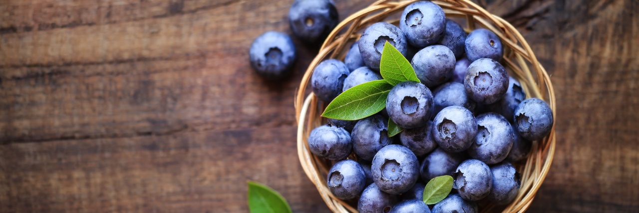 Fresh ripe garden blueberries in a wicker bowl on dark rustic wooden table. with copy space for your text