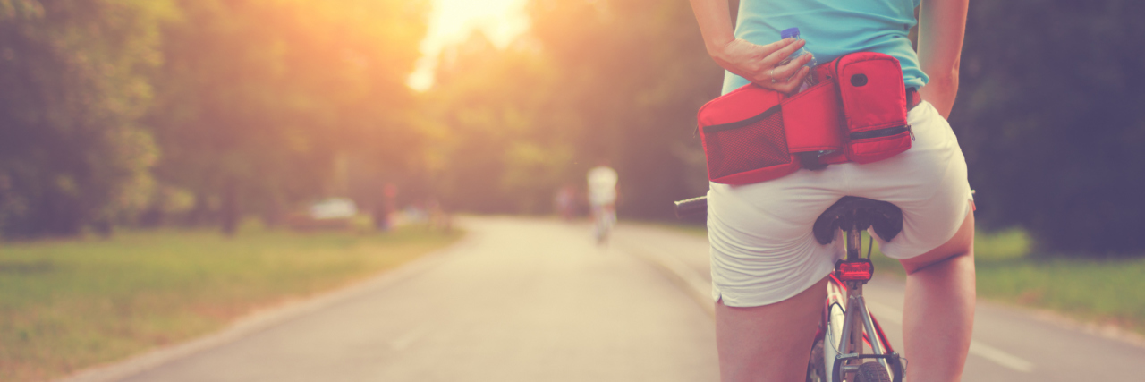 female cyclist on sunlit road stopped for breath with hand on lower back